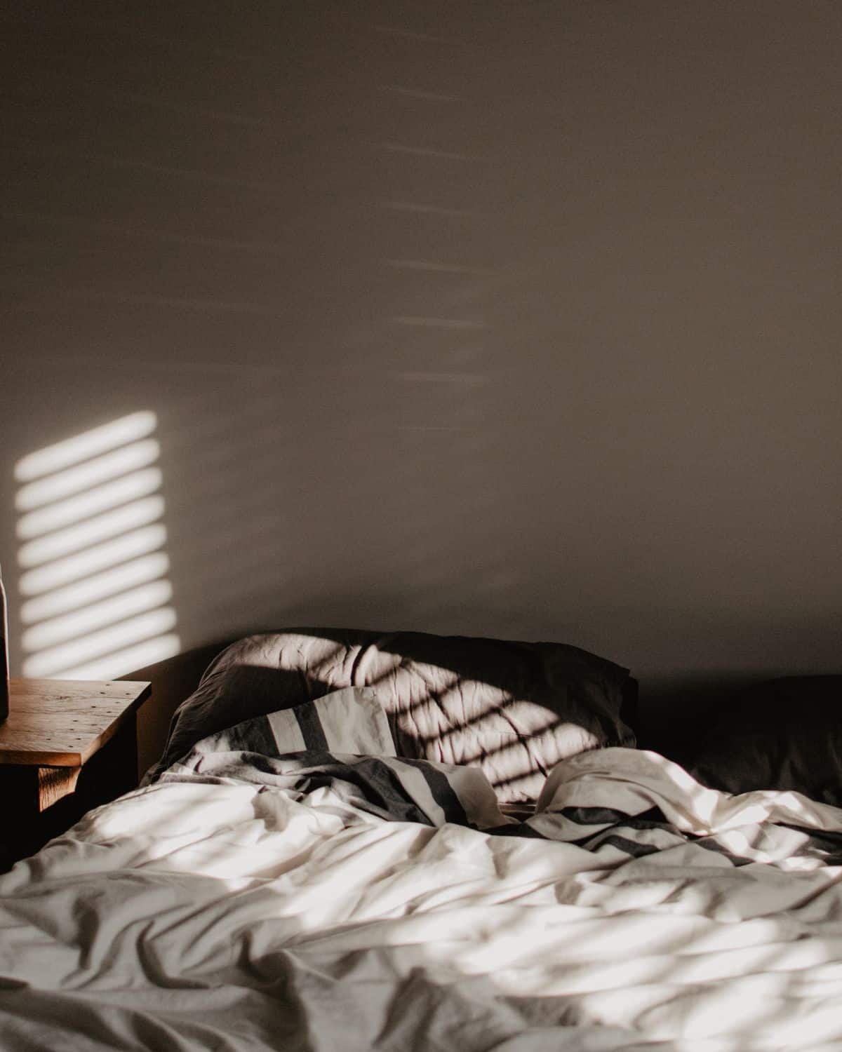 Image of a made bed with sunlight gleaming through a window.