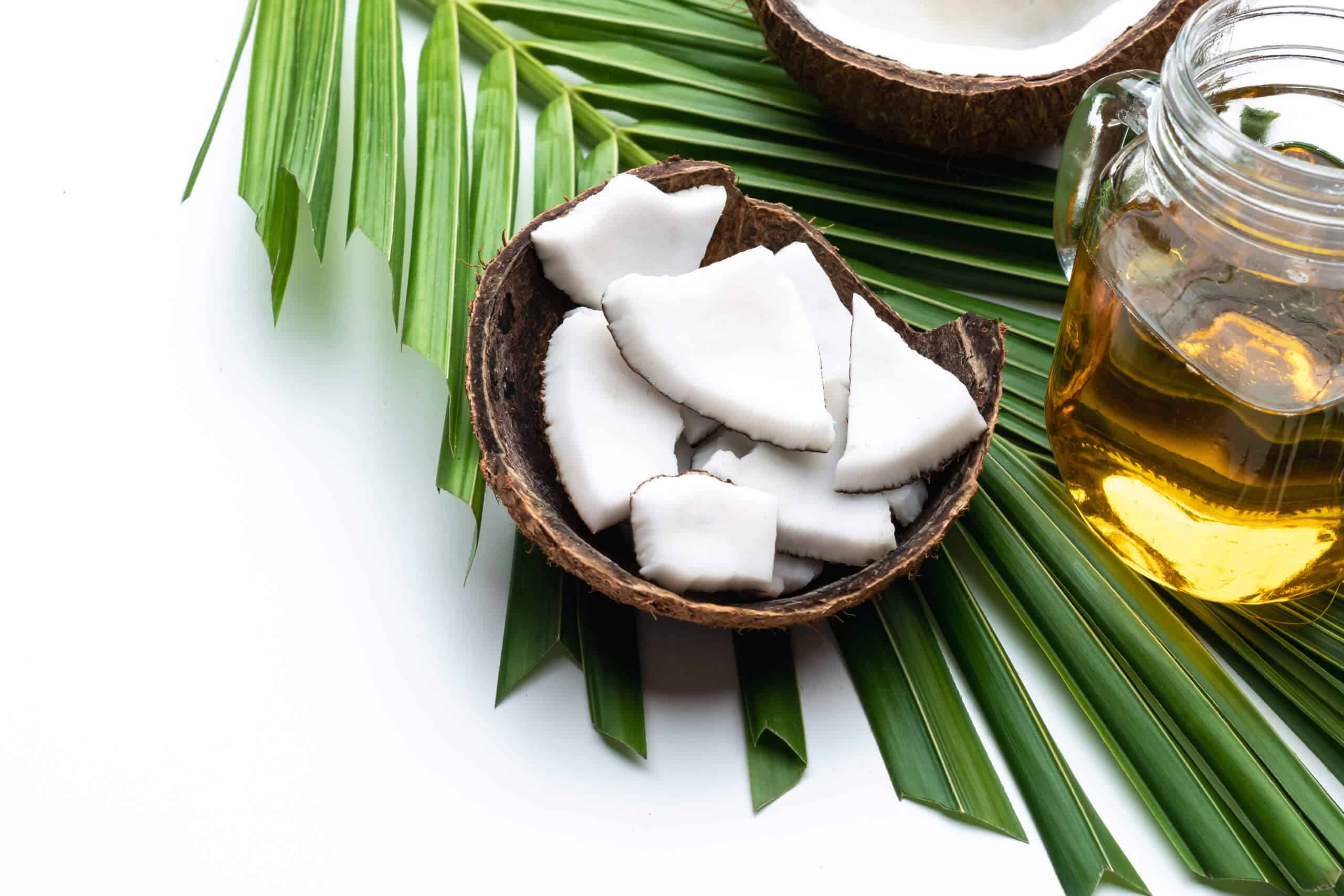 Coconut meat and coconut oil in glass bottle on coconut leaf.