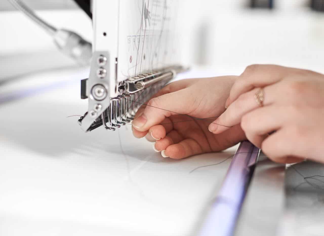Close-up of woman hands filling thread in modern embroidery machine on bright blurred white copy space background. Industrial embroidery, commercial production and high quality results concept.