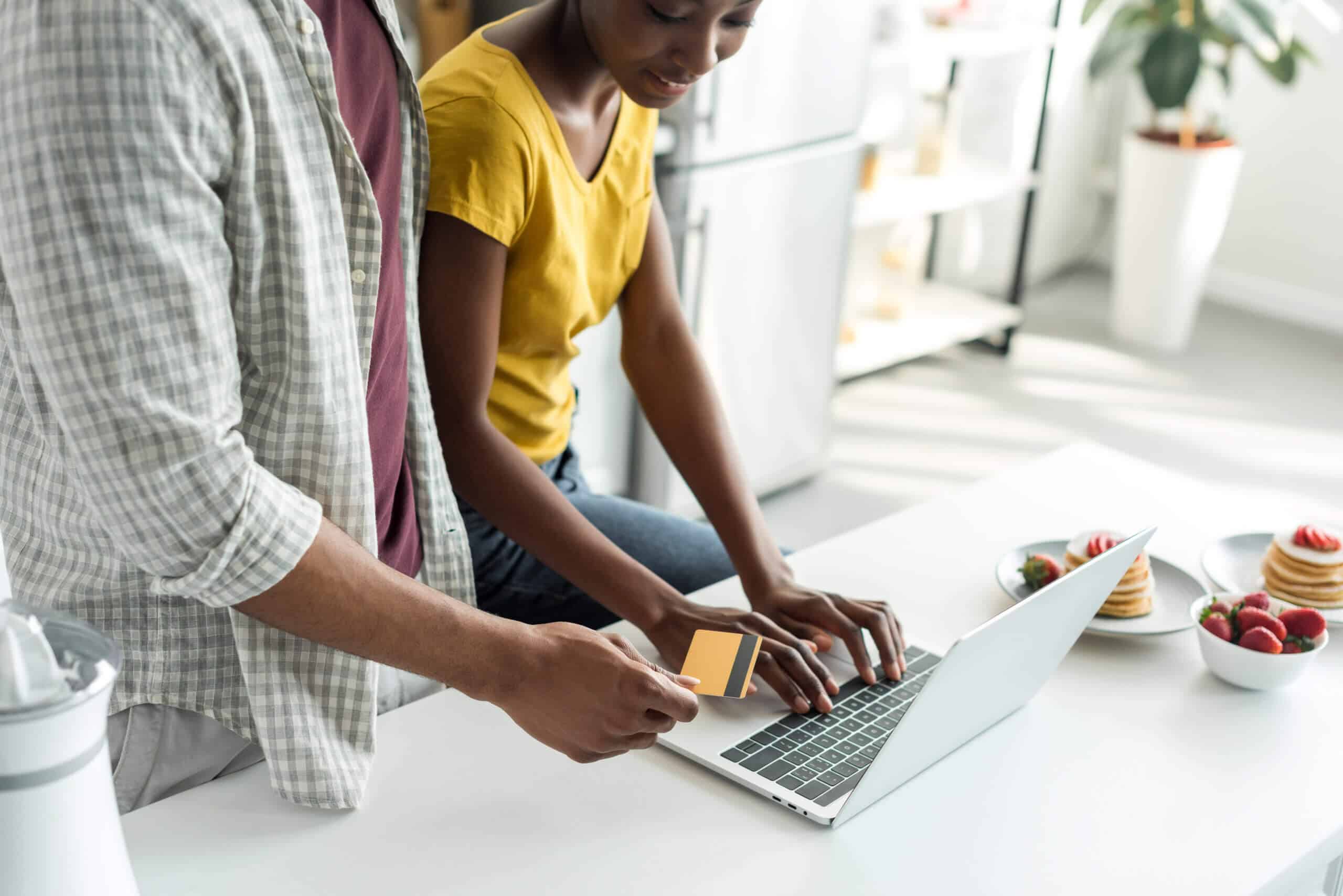 cropped image of african american couple shopping online with credit card and laptop at kitchen