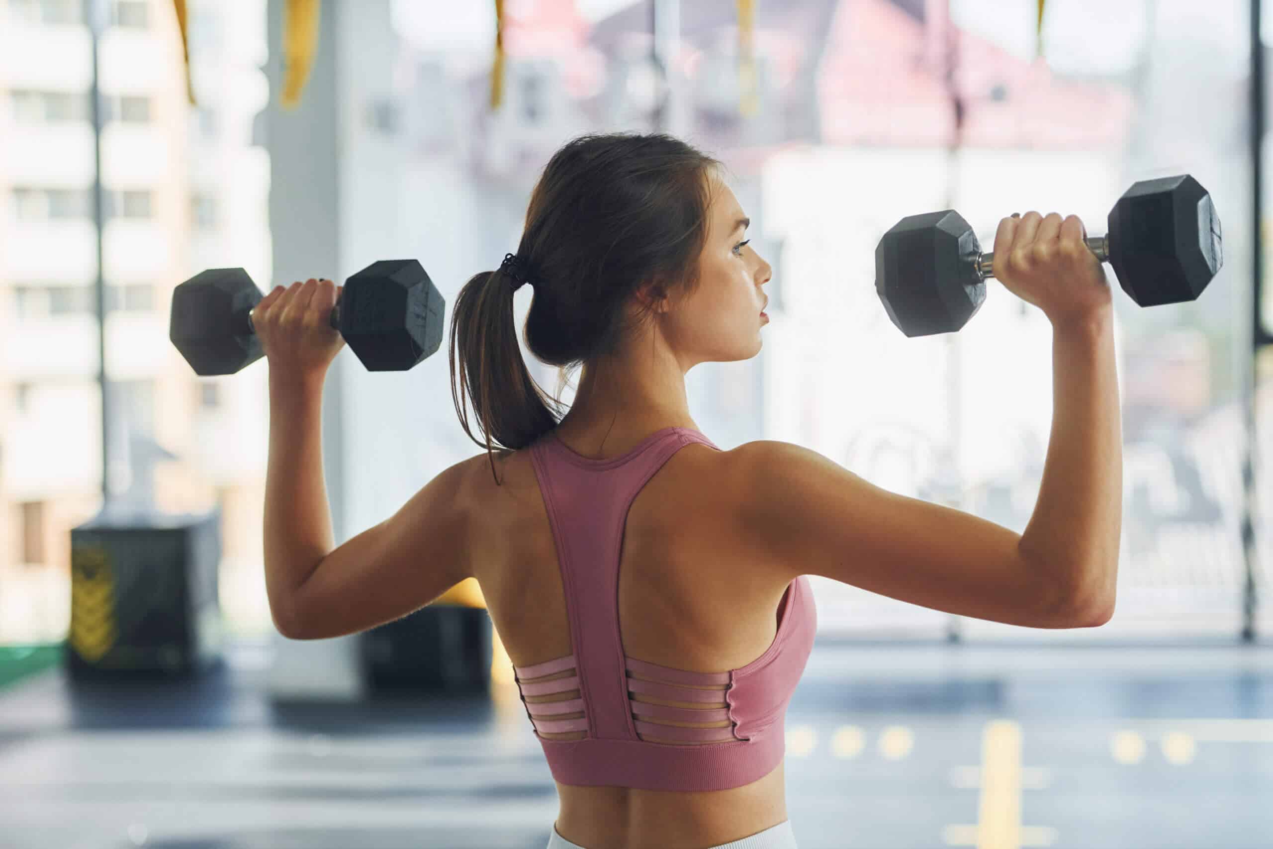 Übungen mit Gewichten. Schöne junge Frau mit schlanker Figur ist im Fitnessstudio.