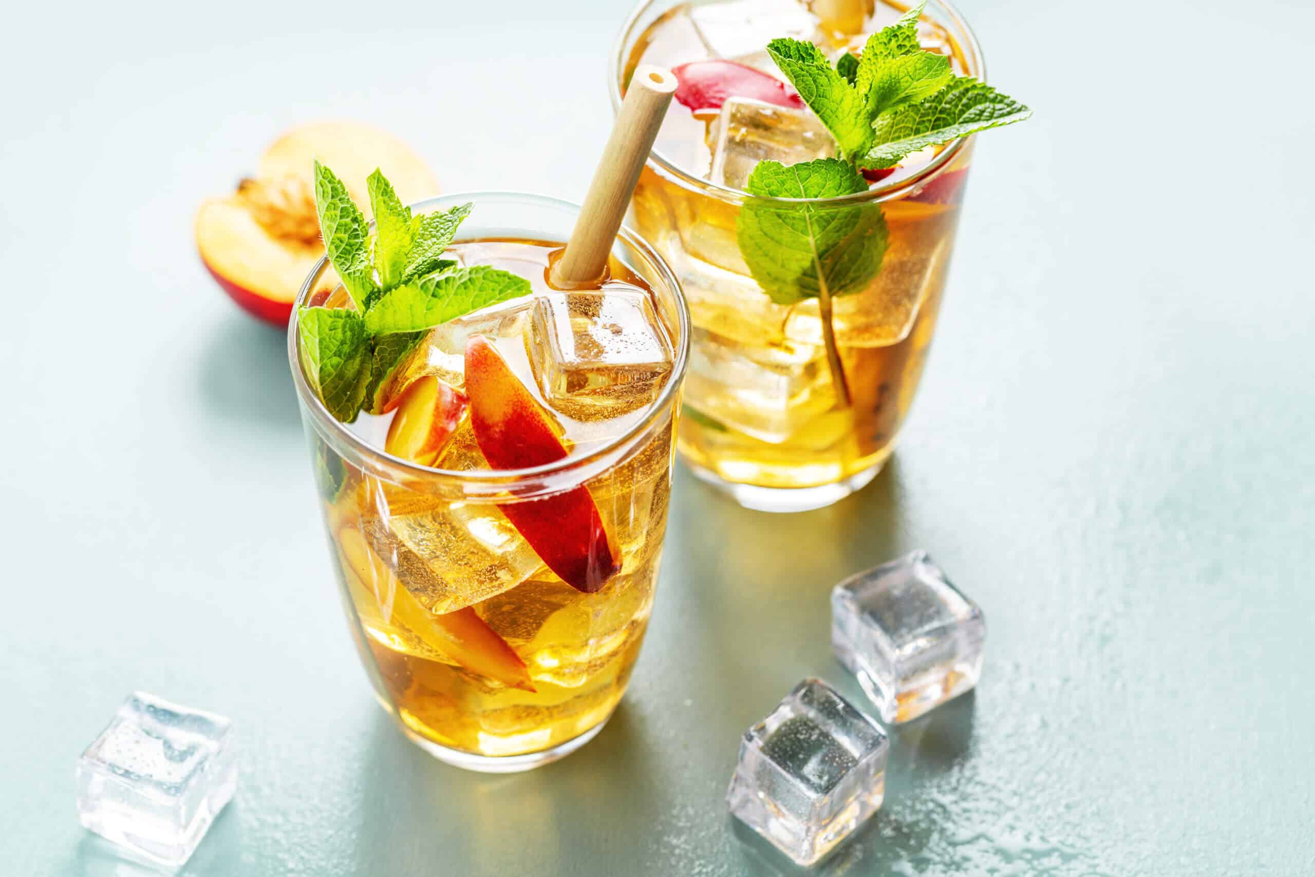 Tasty freshmade iced tea with peach, mint and ice cubes. Served in glasses with bamboo straw.