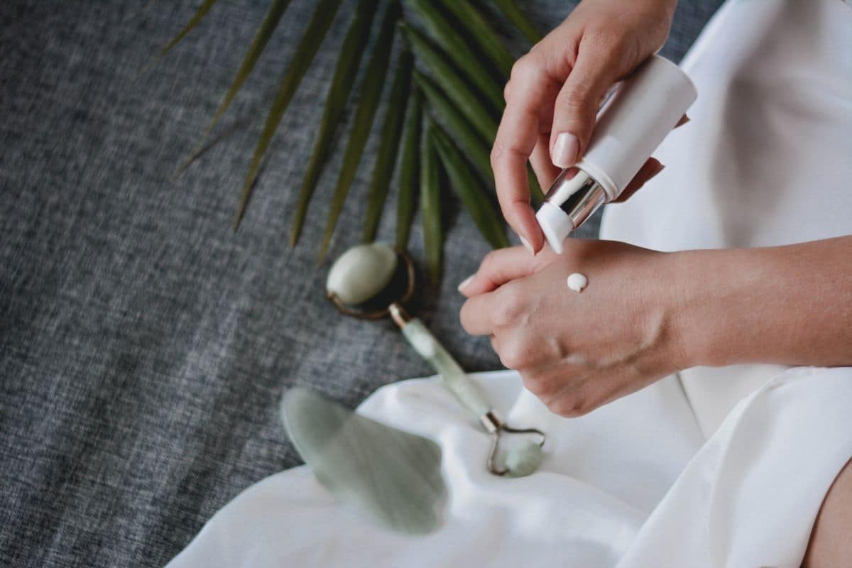 A woman gently applying a dollop of cream to her hand, illustrating a skincare routine.