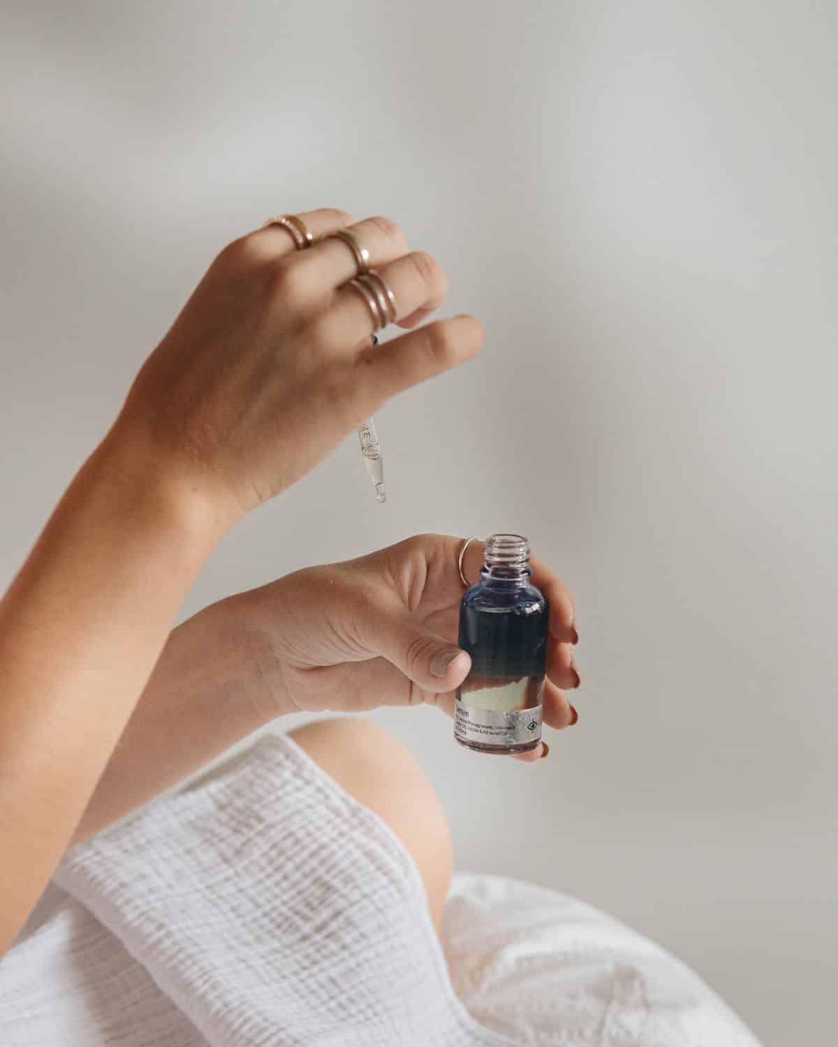 A clear glass bottle filled with face oil, complete with a dropper, set against a minimalist backdrop