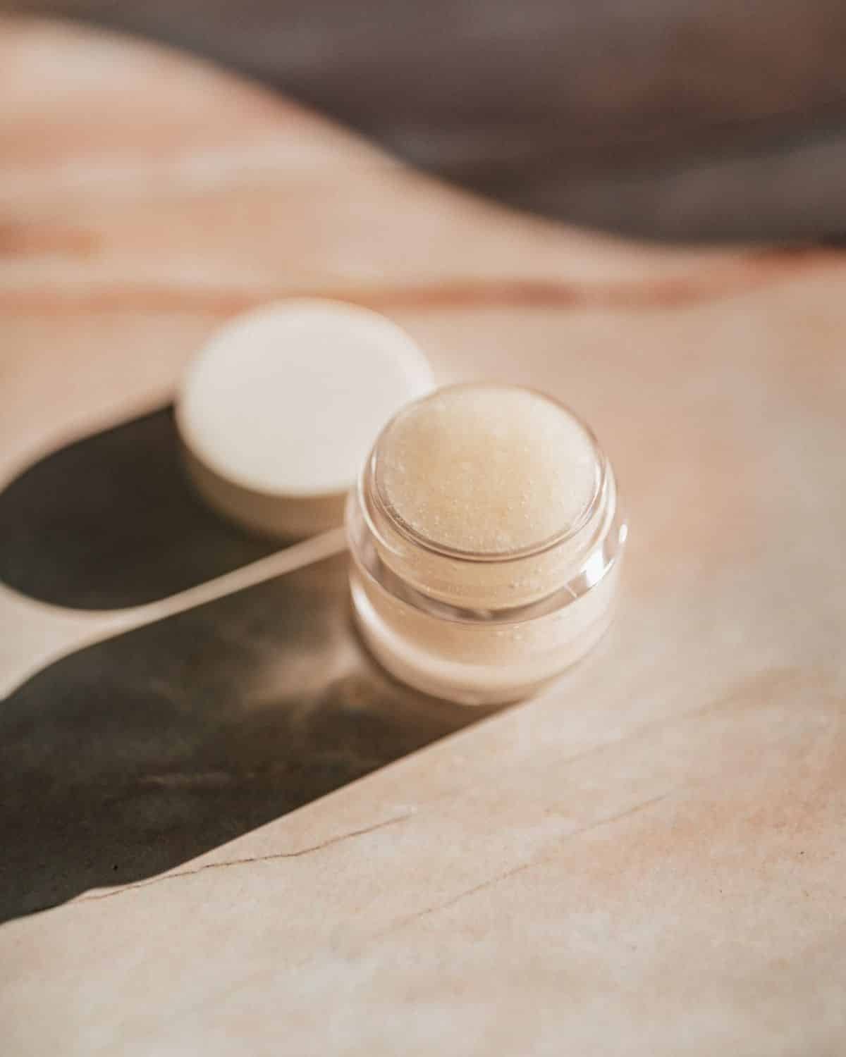 Kleines Glas mit Lippenpeeling mit sichtbaren Granulaten vor einem weichen Hintergrund.