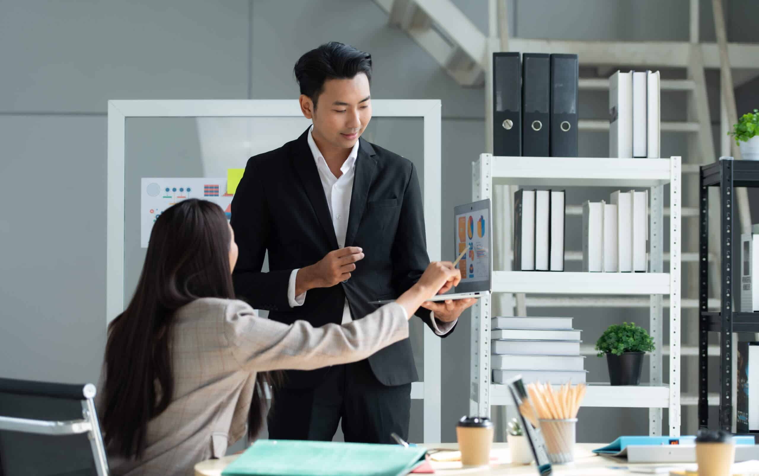 Eine Gruppe junger asiatischer Manager im Bereich Lieferantenmanagement. Das Top-Management trifft sich, um Aktieninvestitionsdaten des Teams in einem Besprechungsraum mit Fenstern und Tageslicht zu überprüfen.