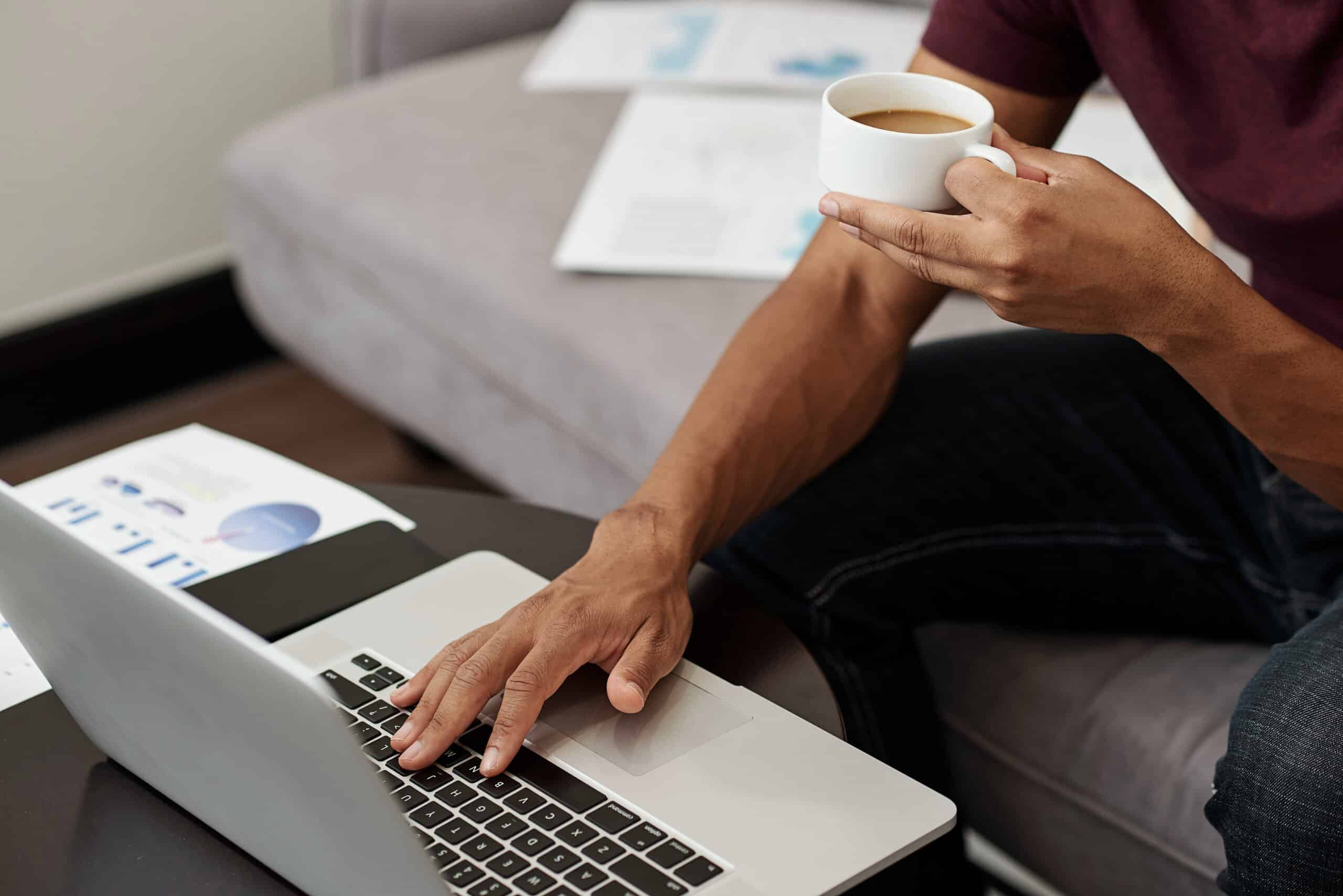 Cropped image of entrepreneur drinking cup of coffee when answering e-mails from clients