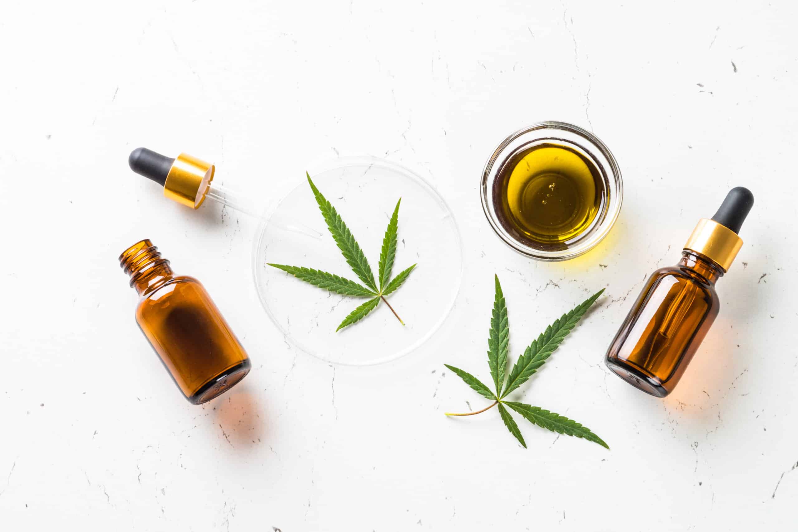 CBD oil and cannabis leaves at white table. Medicine and cosmetic product. Flat lay image.