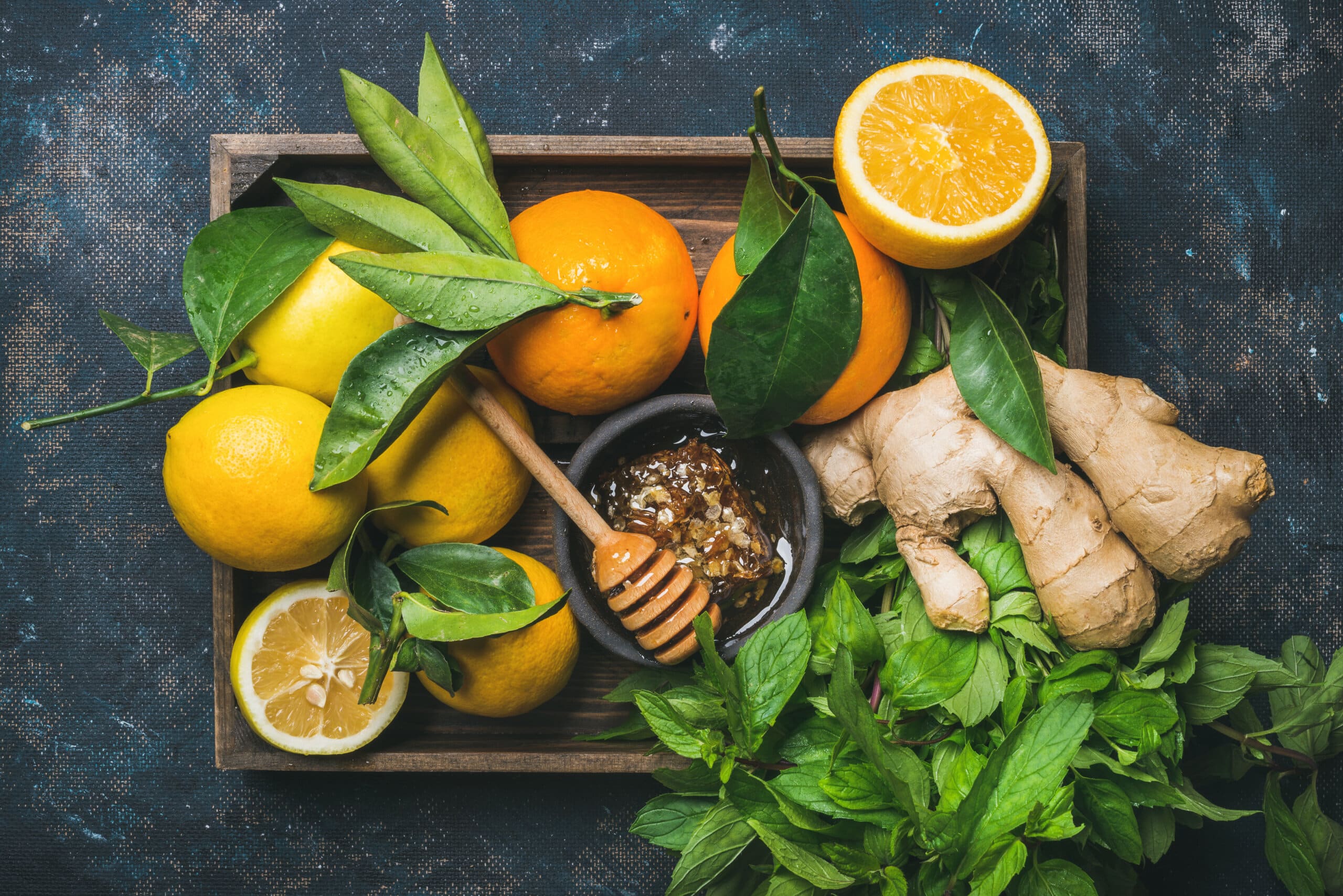 Zutaten zur Herstellung eines immunitätsstärkenden natürlichen Getränks. Zitronen, Orangen, Minze, Ingwer, Honig in einer Holzkiste auf einem Sperrholzhintergrund, Draufsicht. Clean Eating, gesunder Lebensstil, Detox, Diätkonzept