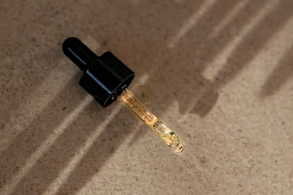 A clear glass bottle filled with face oil, complete with a dropper, set against a minimalist backdrop