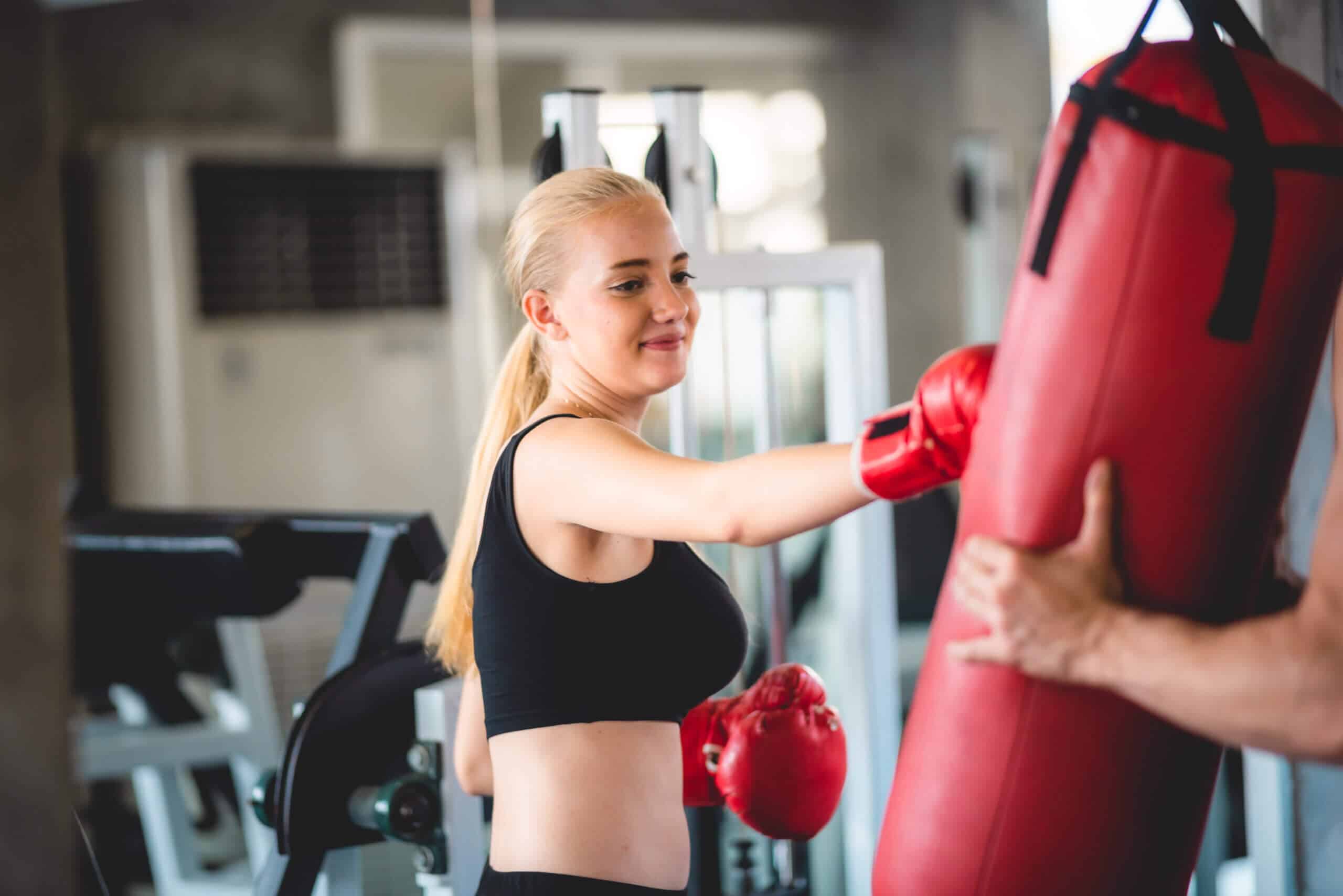 Starke junge Sportlerin beim Kickbox-Training mit Handschuhen und Trainer bei einer Fitness-Private-Label-Marke 