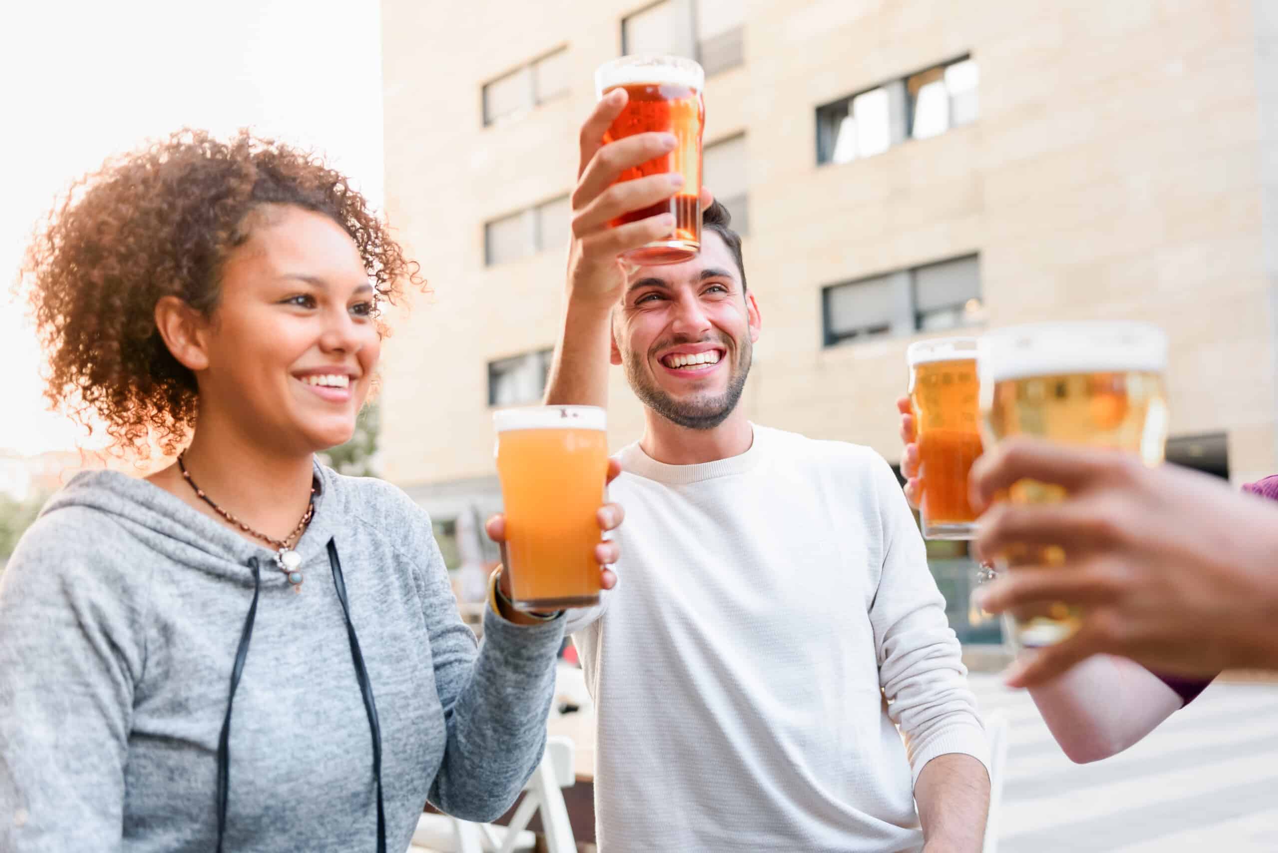 Group of happy friends clinking glasses of beer while sitting on terrace of cafe in city and spending time together
