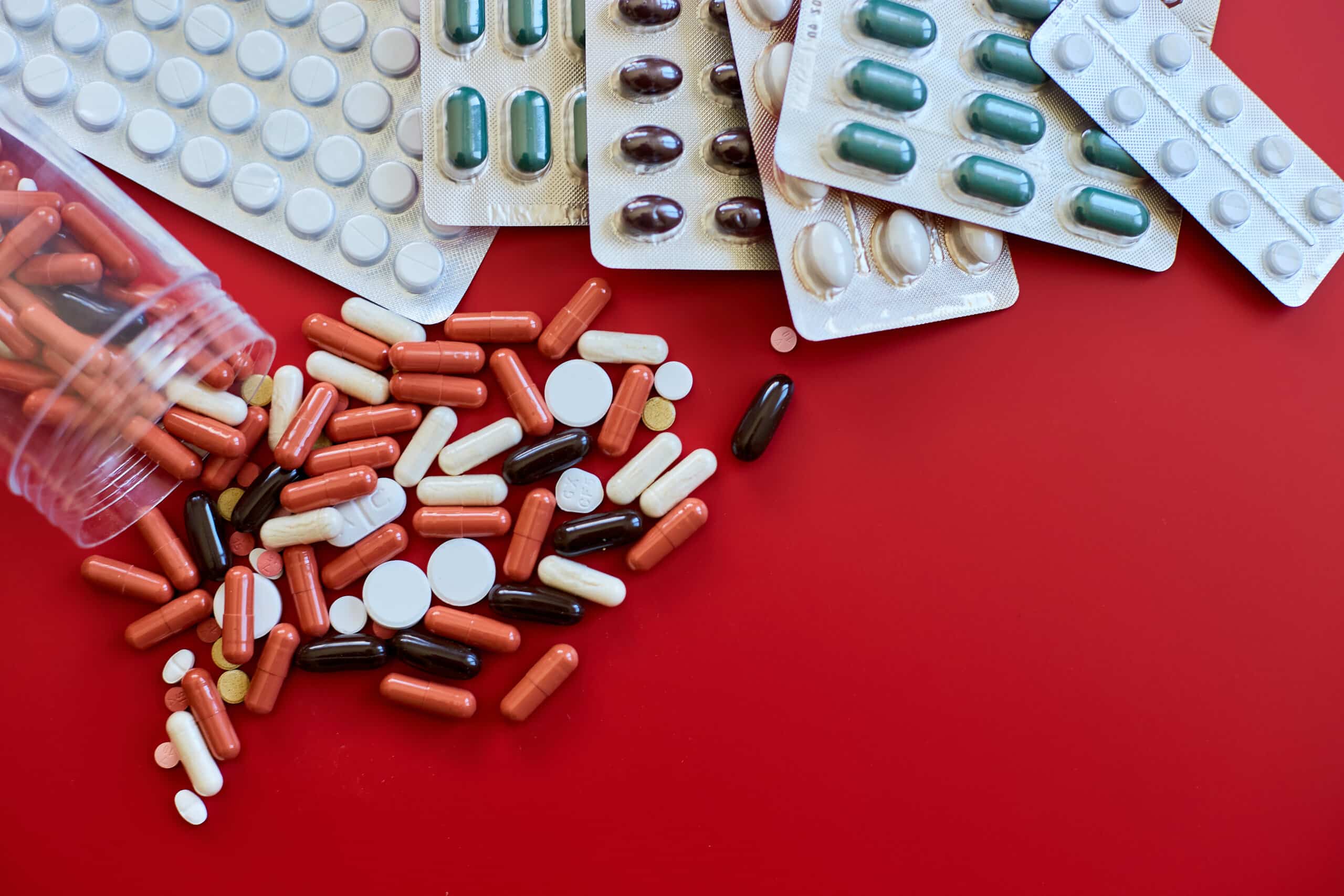 Flat lay different colorful probiotics pills on red background, Vitamin deficiency, avitaminosis concept, assorted pharmaceutical medicine pills, Dietary supplement healthcare product.