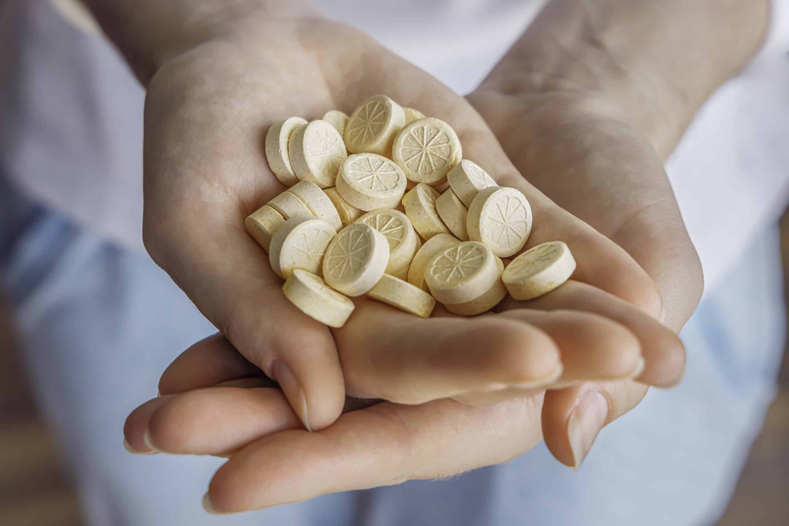 A woman holds vitamins pills in her hands. Vitamin C provides an essential nutrient for healthy bones, cartilage, teeth, and gums. An antioxidant for the maintenance of good health, vitamin C helps in connective tissue formation, wound healing, and to metabolize fat and protein.