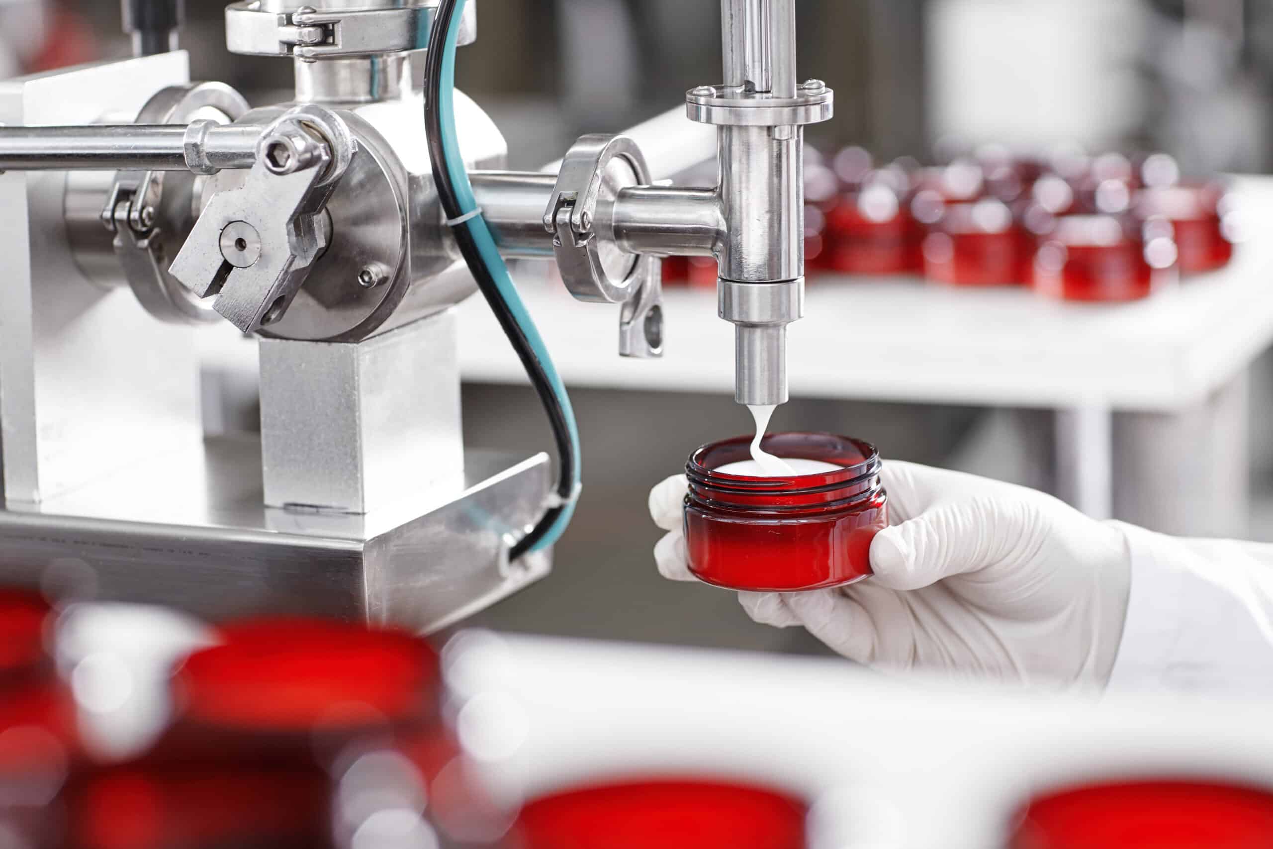 Produktion und Verpackung von Kosmetikprodukten. Nahaufnahme eines Fabrikarbeiters mit Handschuhen und Kittel, der ein Plastikgefäß hält und es mit weißer Gesichts- oder Körpercreme füllt. Schönheit, Hautpflege und Kosmetologie