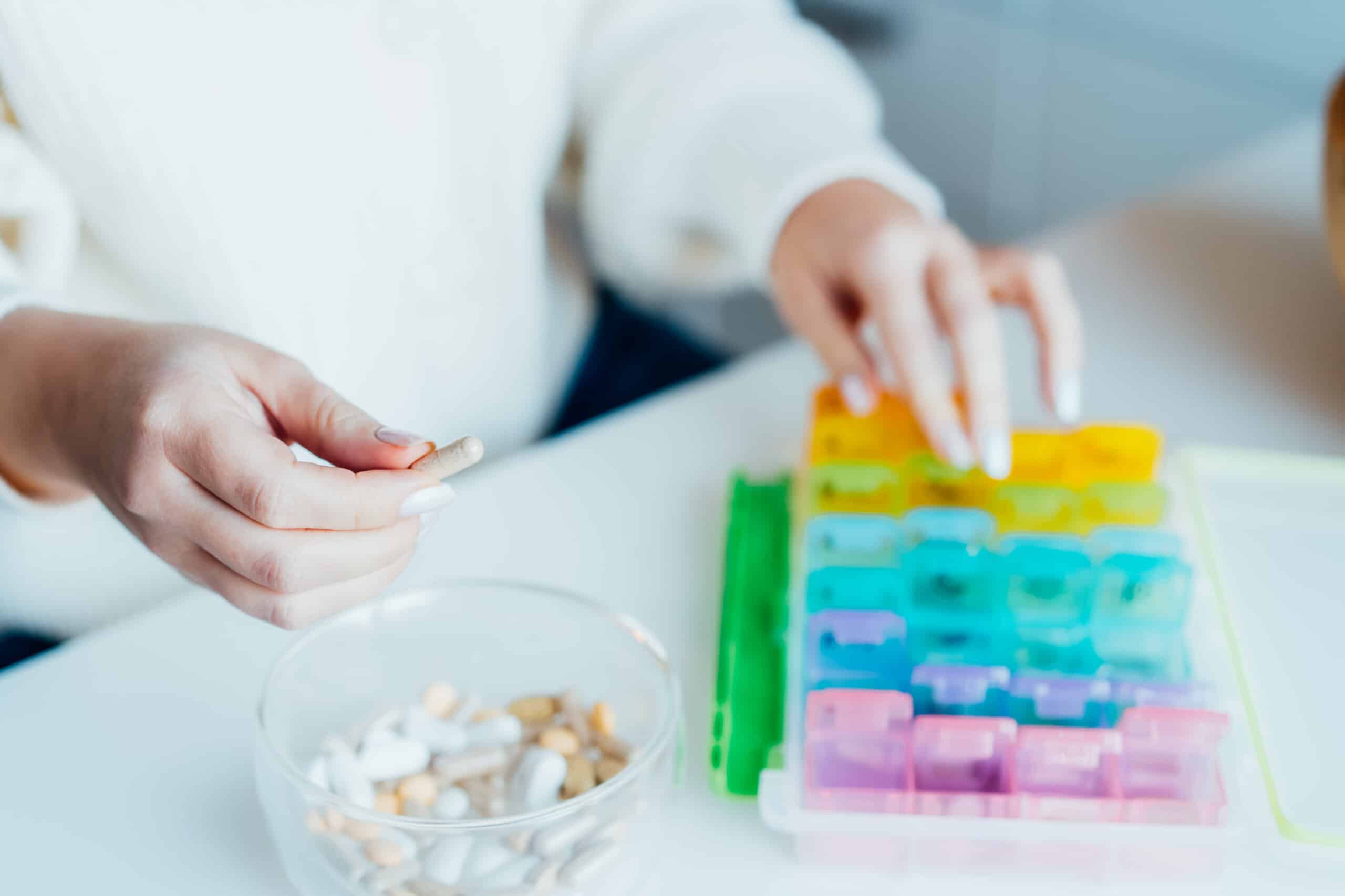 Woman's hands sorting pills into pills organizer. Close up medical pill box with daily doses of medicines. Antioxidant diet vitamin supplements for health and beauty care, biohacking concept