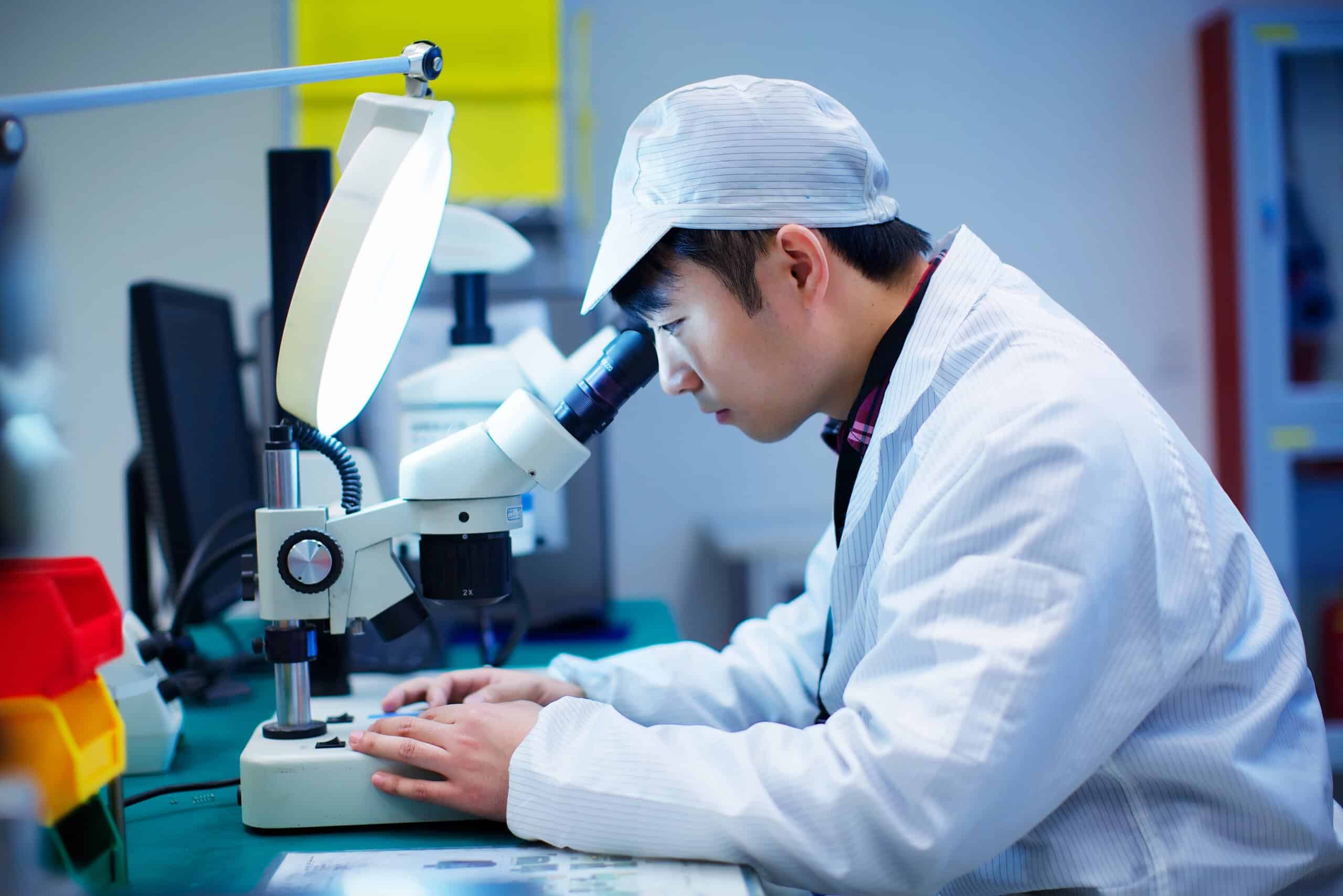 Arbeiter in einer Fabrik für Kleinteile in China blicken durch ein Mikroskop