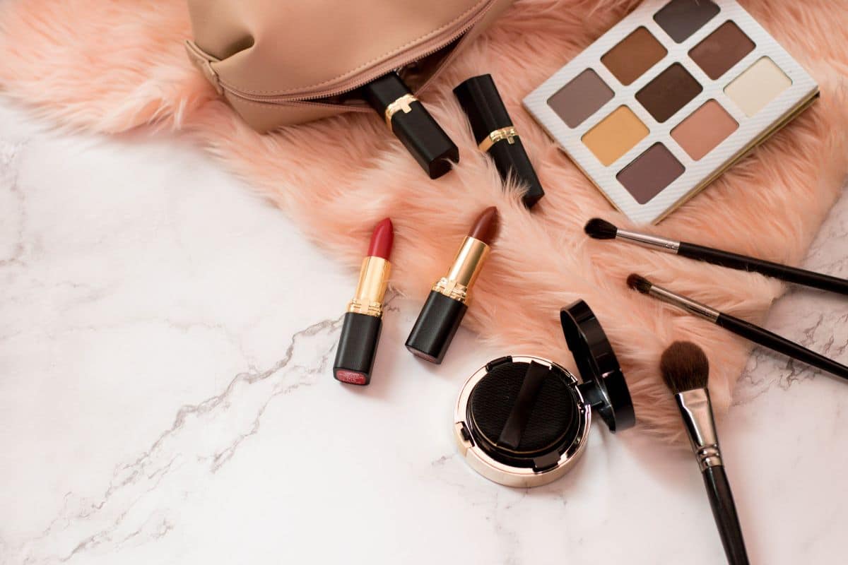 Verschiedene Make-up-Produkte, darunter Lidschatten, Lippenstifte und Pinsel, auf einer flachen Oberfläche ausgebreitet.