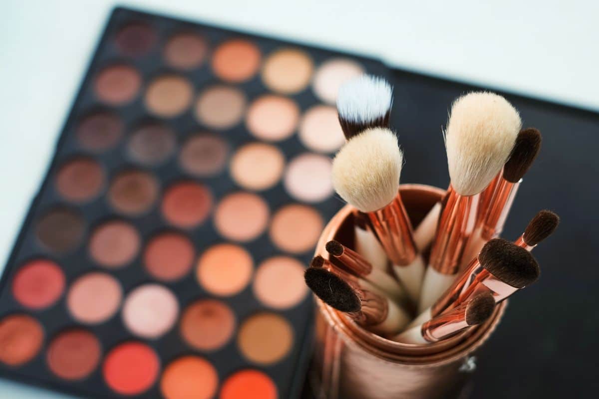 Bild, das eine Vielzahl von Lidschatten in verschiedenen Farbtönen zeigt, kombiniert mit einer Auswahl an professionellen Make-up-Pinseln.