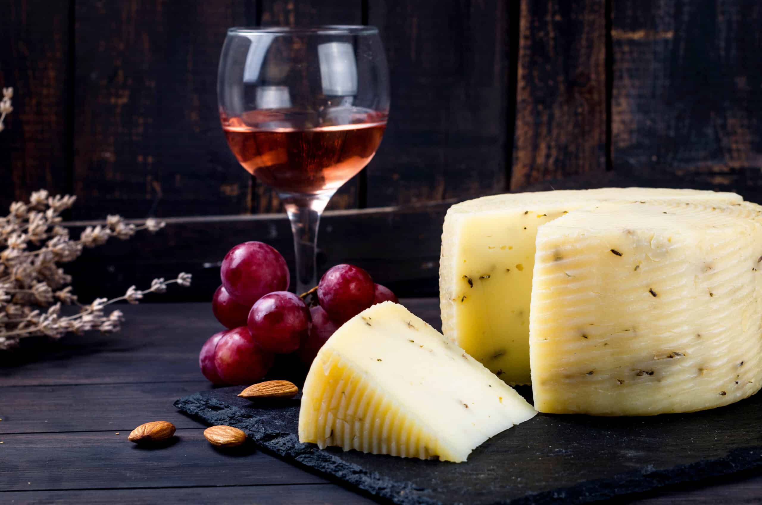 homemade cheese head with lavander on old dark wooden board and glass of wine on table. Fresh dairy product, healthy organic food. Delicious appetizer.