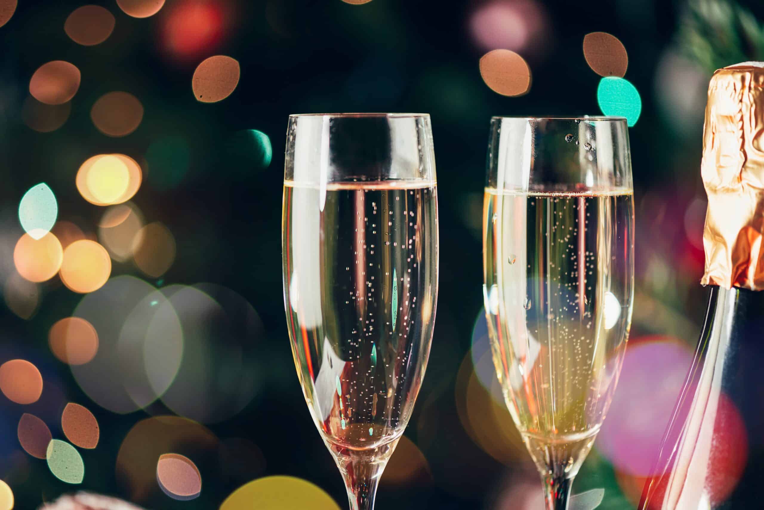 Two flute glasses and bottles of champagne in preparation for Xmas or New Year party. One bottle is in the christmas jumper and xmas tree on the background