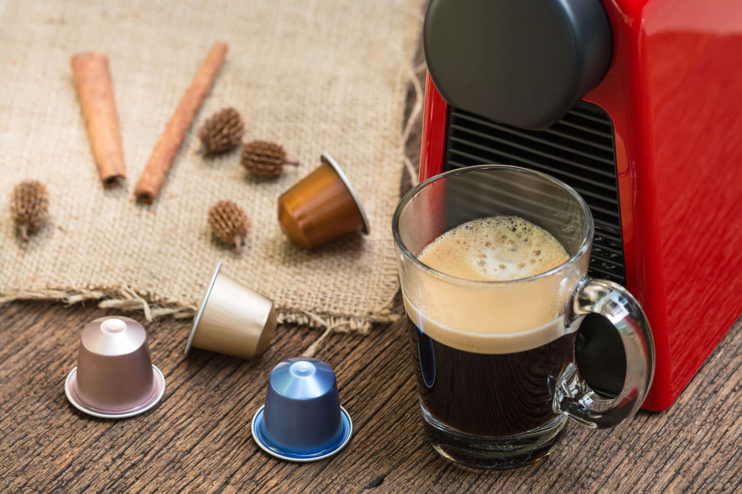 Espresso coffee machine with capsules making coffee in a glass cup on the wooden table.