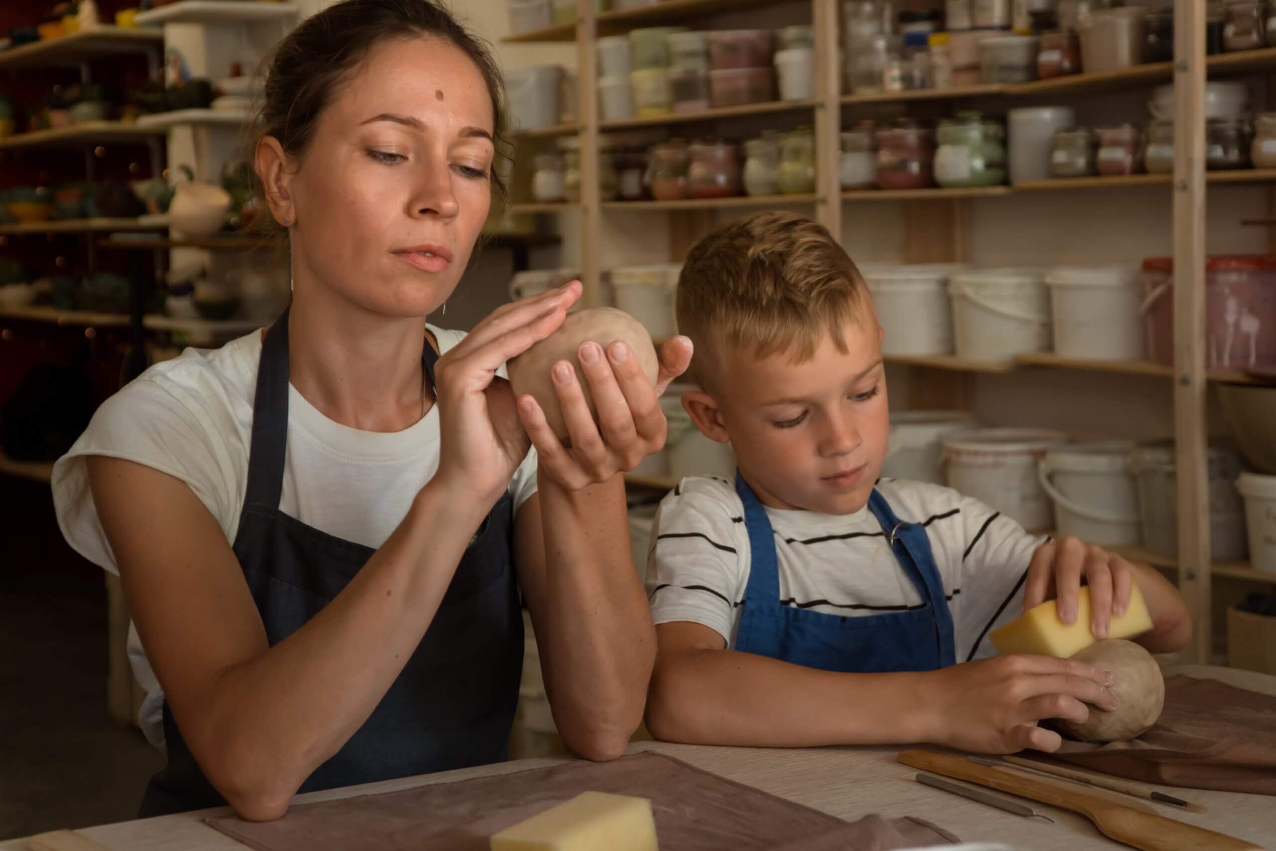 Senior man showing the woman how to make form of vase from clay on pottery wheel in studio