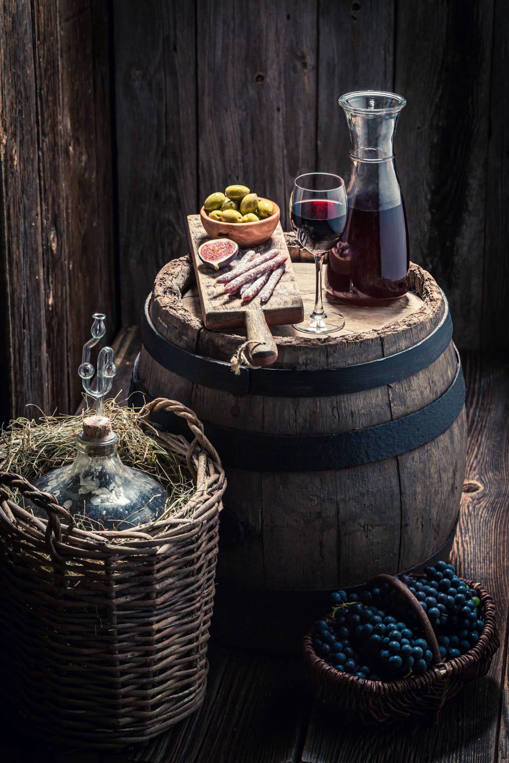 Red wine with snacks and demijohn in basement. Homemade wine industry.