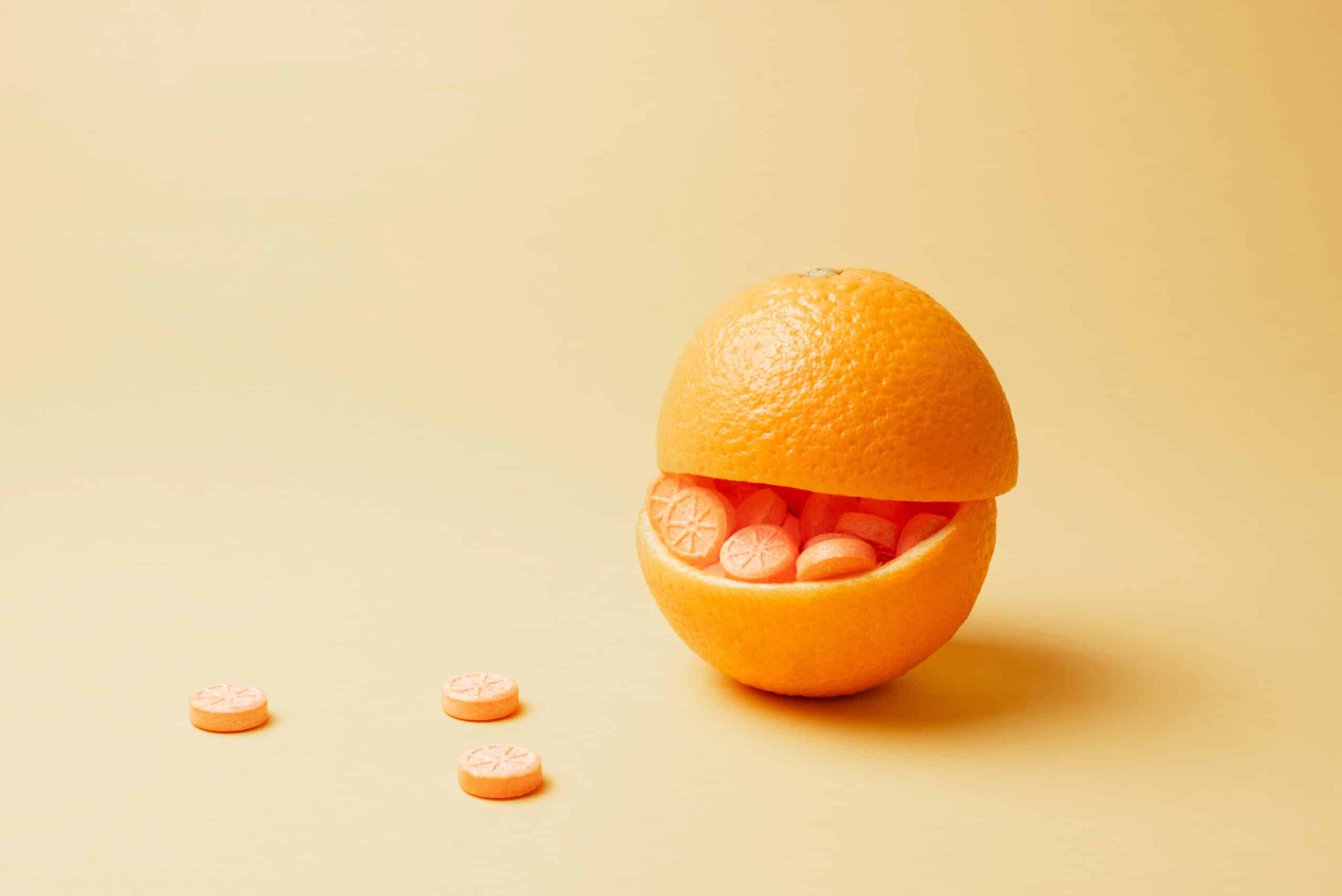 Orange gefüllt mit orangefarbenen Pillen auf gelbem Hintergrund. Vitamin-C-Pillen als Alternative zu Zitrusfrüchten. Konzept zur Stärkung des Immunsystems.