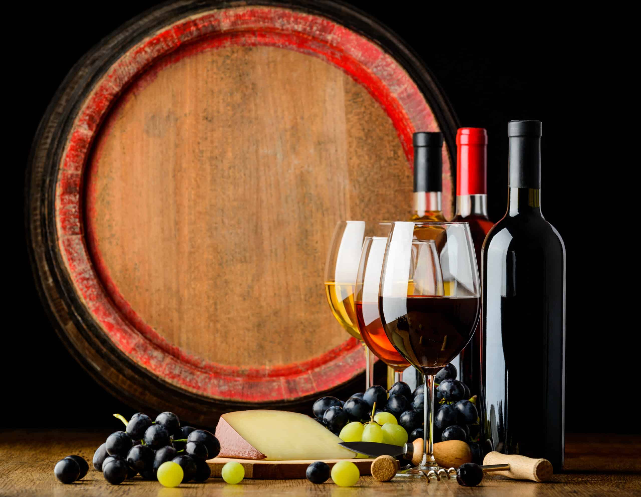 Wine bottles and glasses of white, rose and red wine on a wooden table with grapes and cheese
