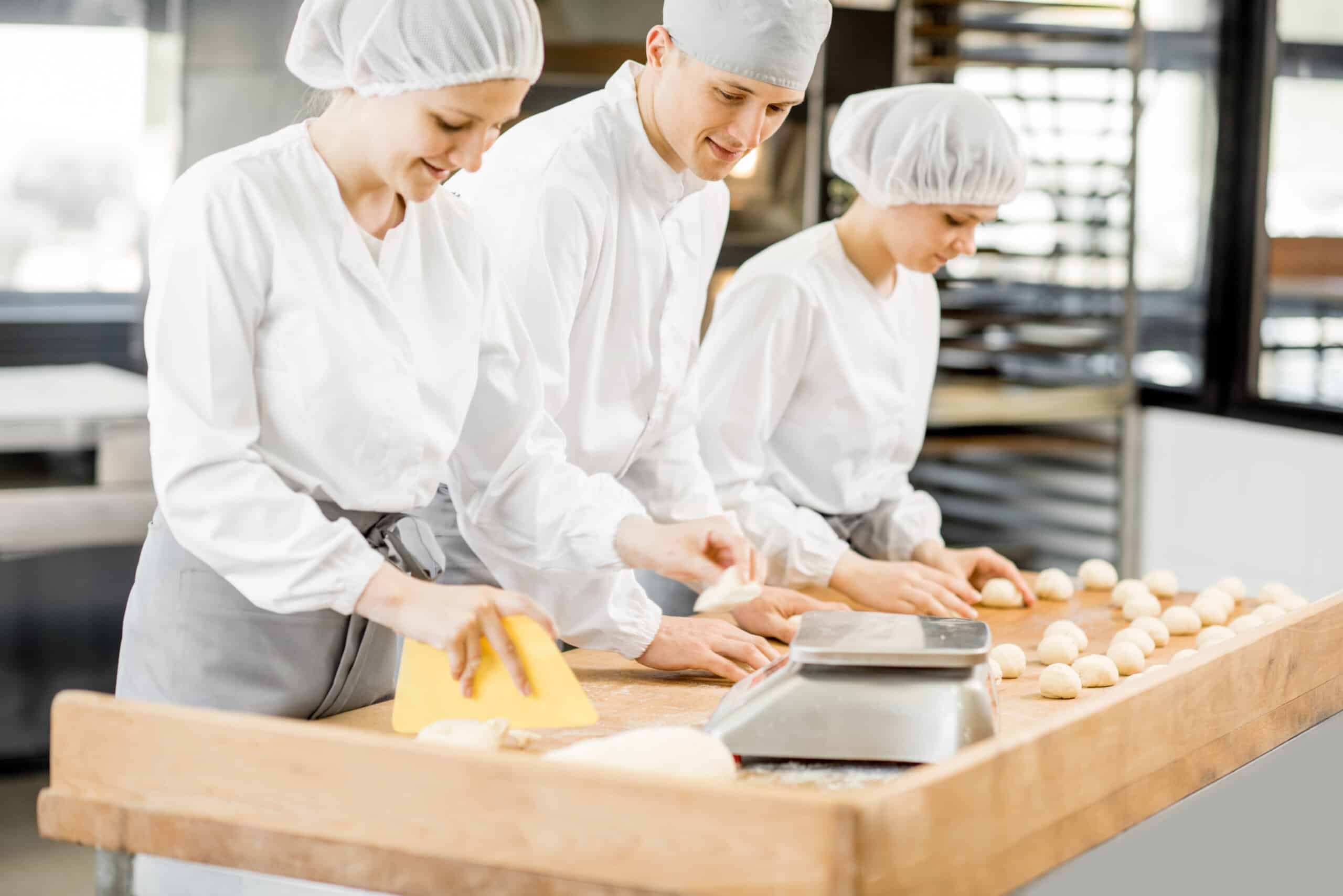 Three bakers having fun forming dough for baking standing together at the modern manufacturing