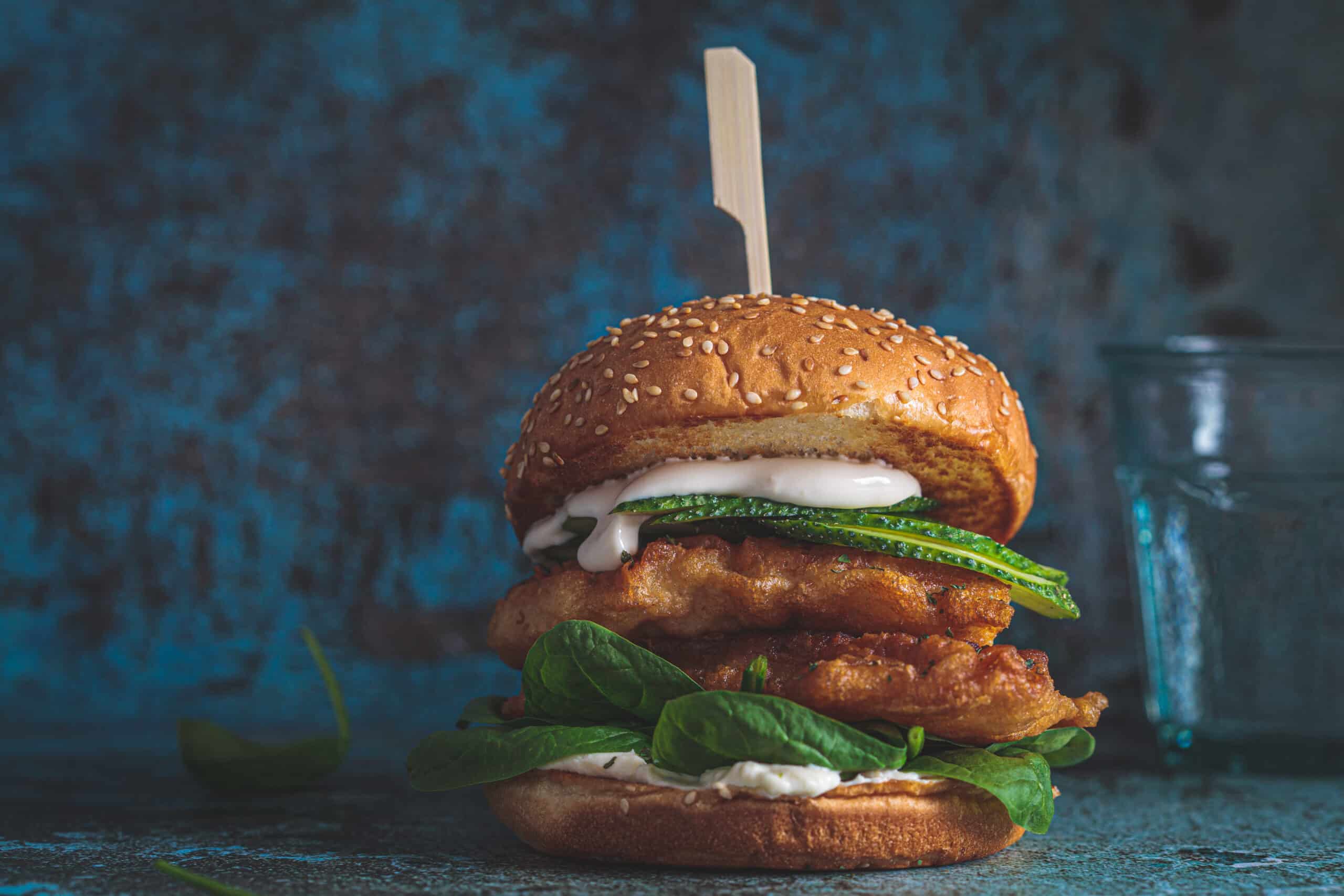 Fish burger on gray plate, dark blue background, copy space. Cod fish in batter with mayonnaise and spinach sandwich.