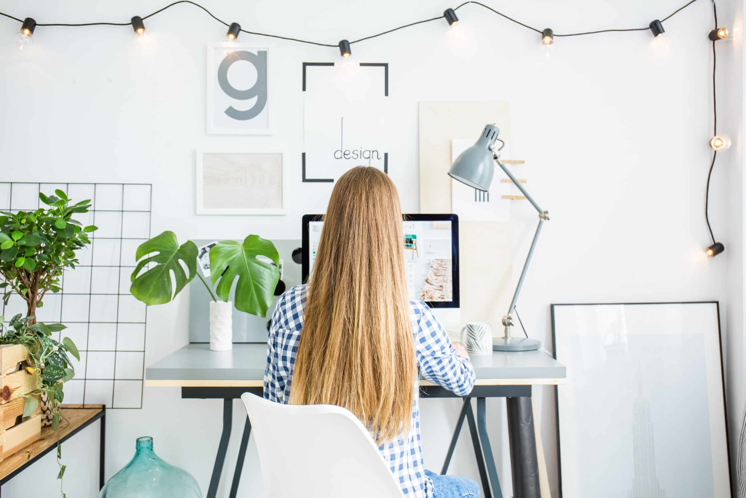 Person with long curly hair sits at a desk with a flower and designs on a laptop