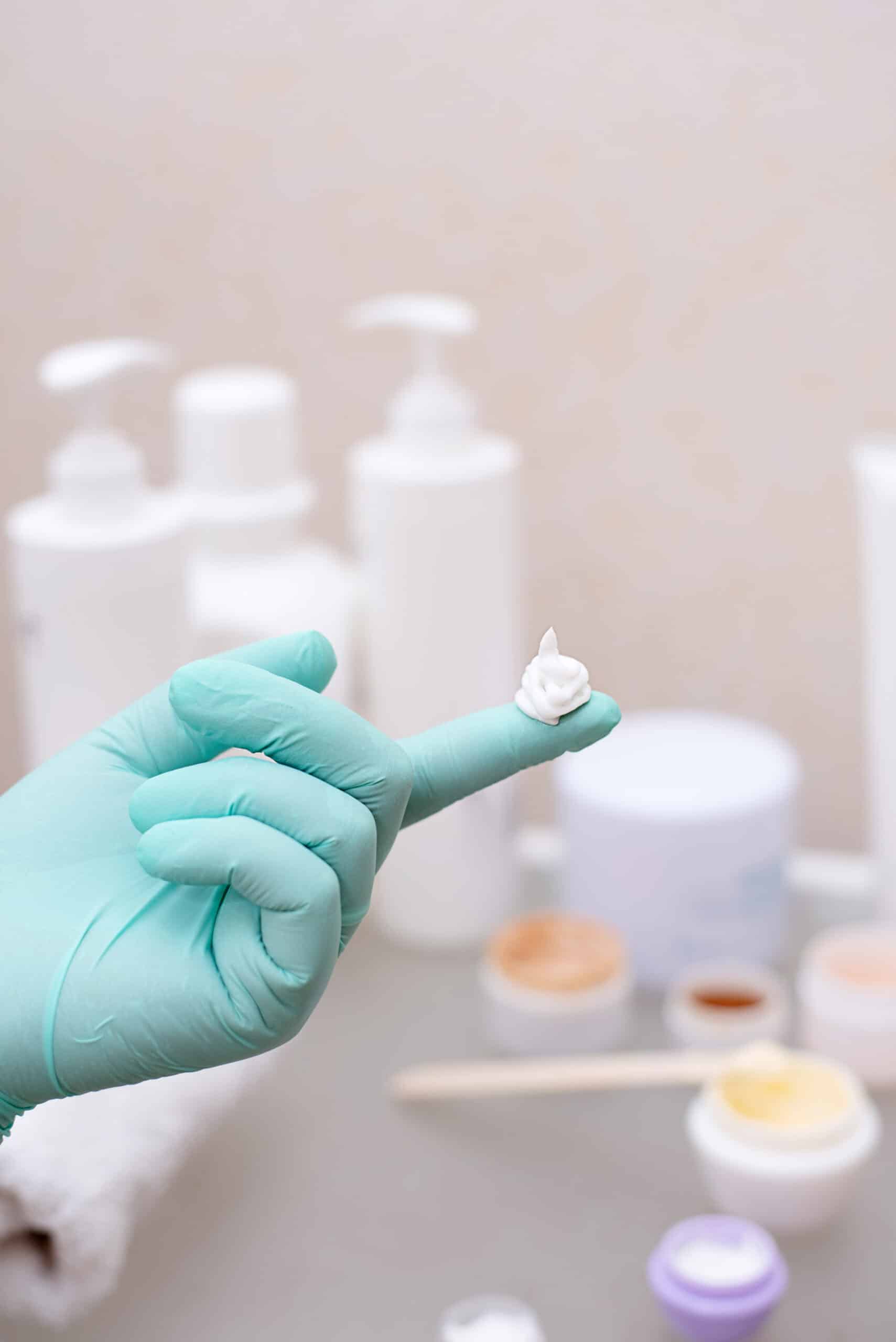 A drop of cream on a hand in a medical glove on the background of a table with jars of cream, skin care concept, close up.
