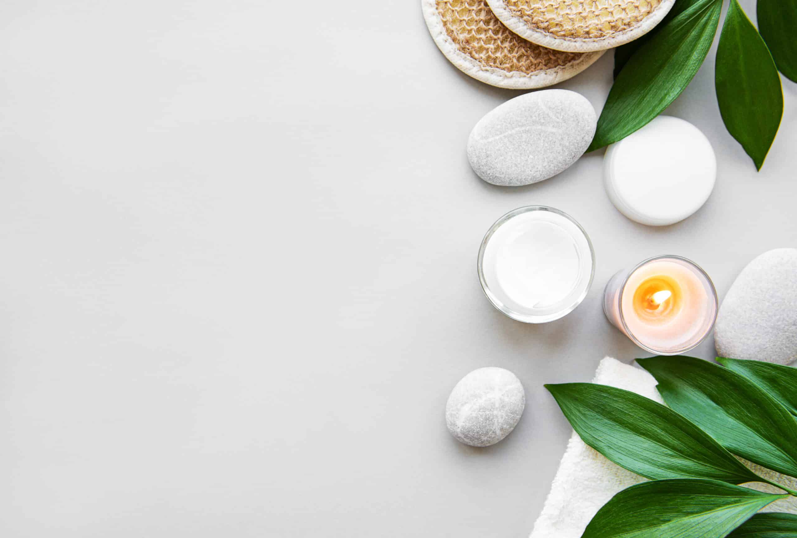 Spa concept, green leaves, candles and moisturizer cream on white background. Flat lay