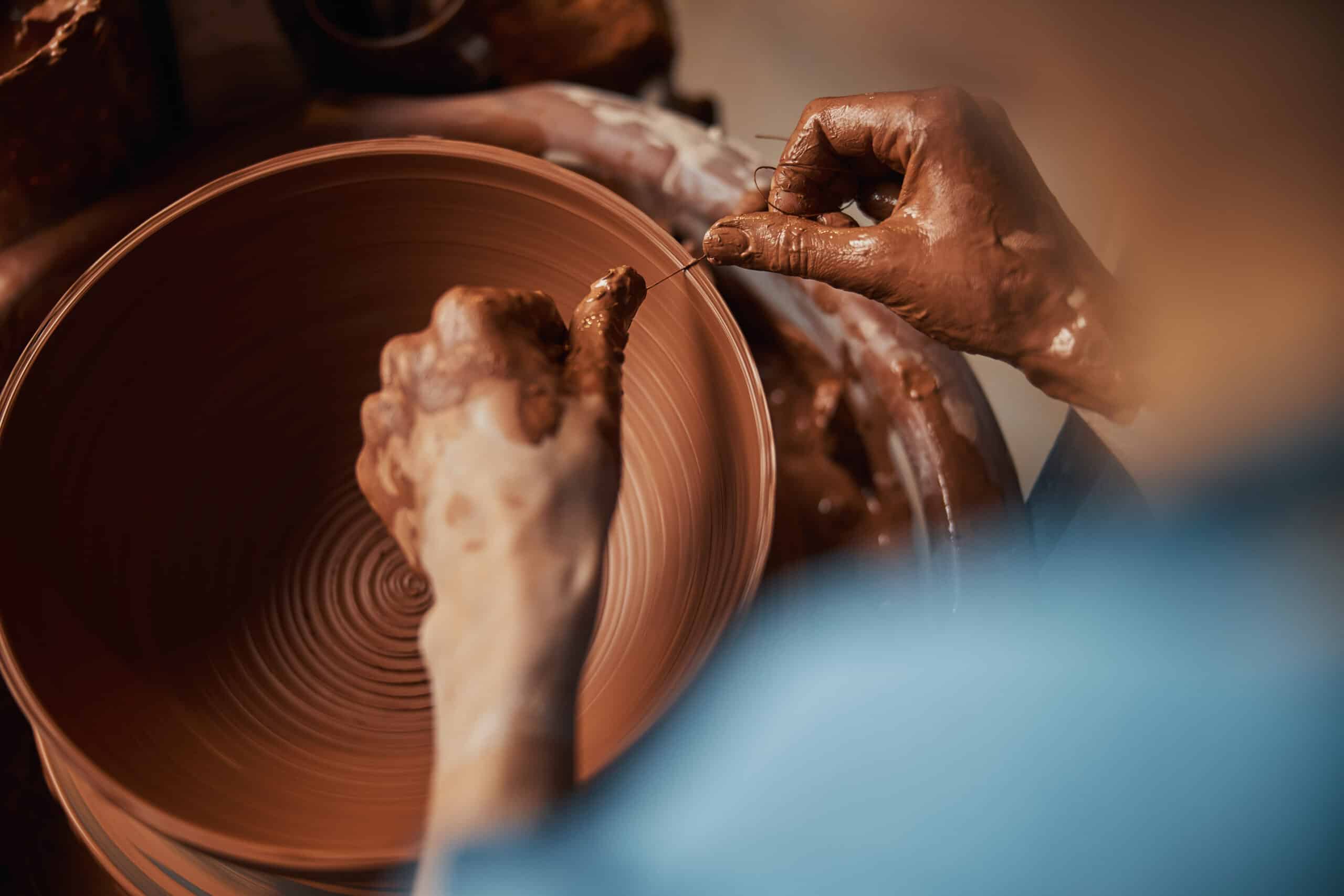 Close up top view portrait of female hands holding special thread and creating texture on clay bowl in art studio
