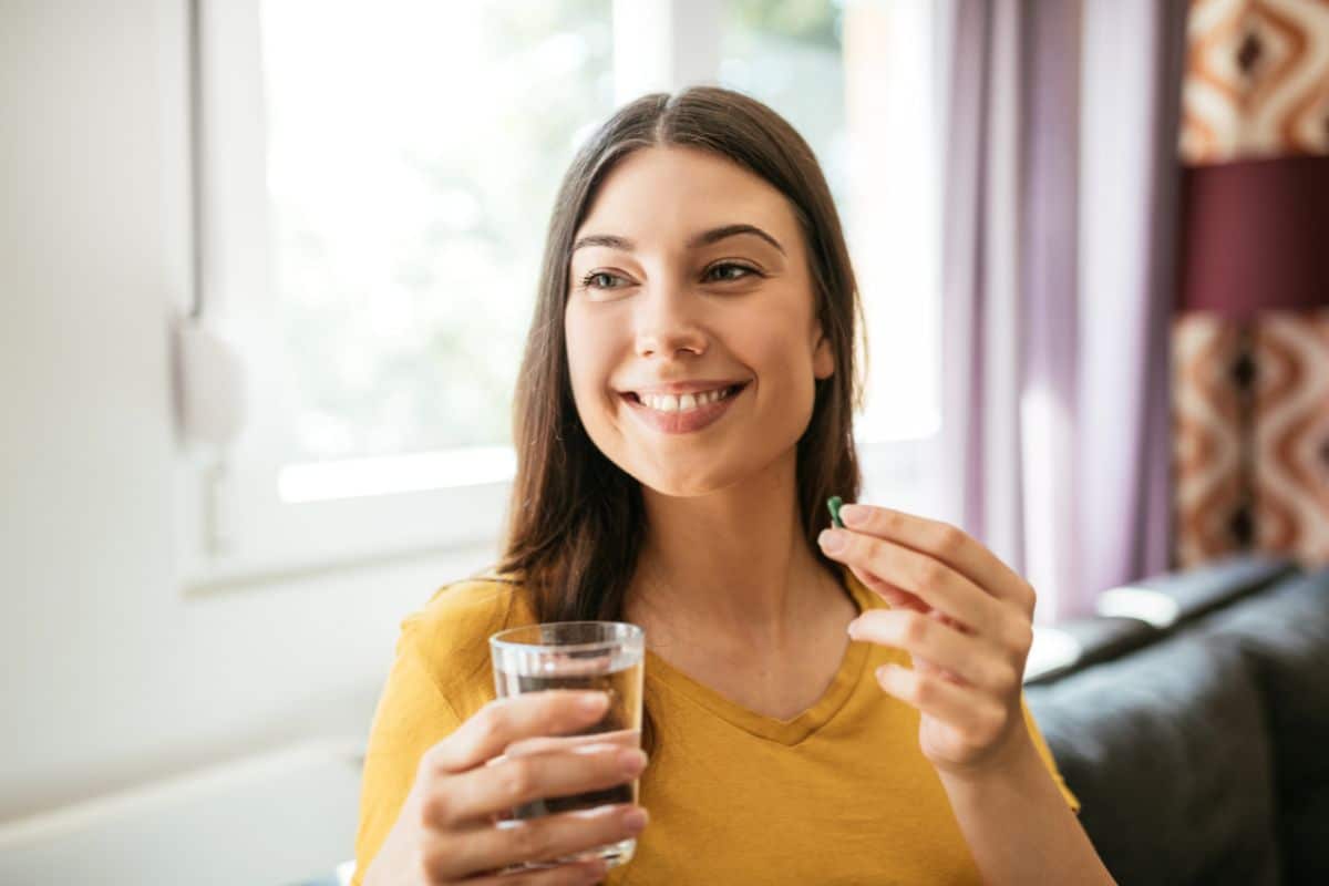 Eine Frau, die eine Nahrungsergänzungsmittelkapsel mit einem Glas Wasser einnimmt.