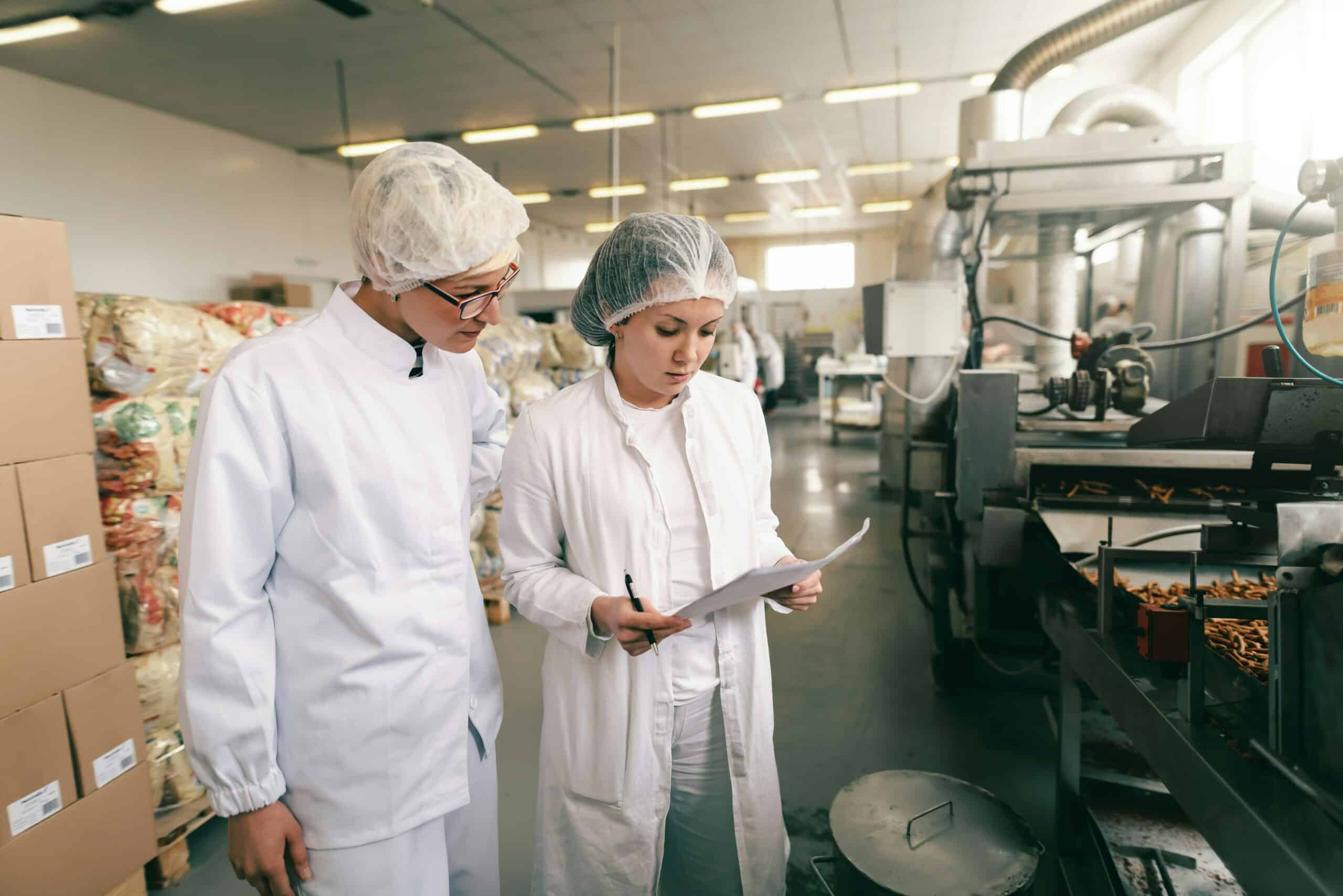 Lohnhersteller für Nahrungsergänzungsmittel: Zwei Personen überprüfen Notizen oder eine Checkliste in einer Fabrikumgebung.
