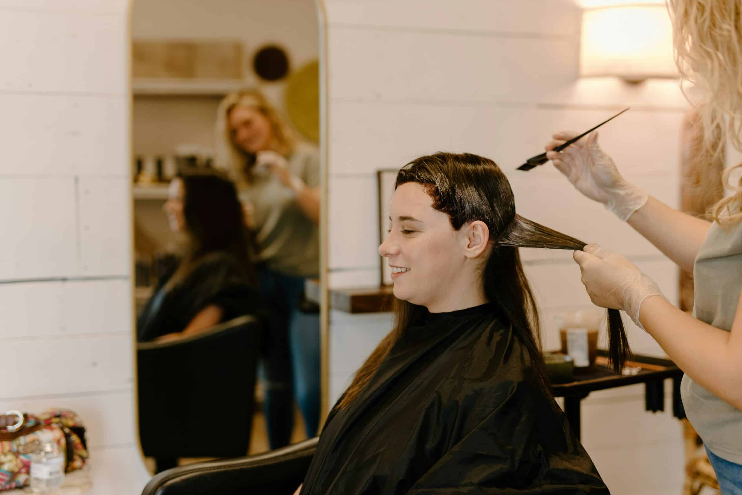 Eine Frau lässt sich von einer Stylistin die Haare mit pflanzlicher Farbe braun färben.
