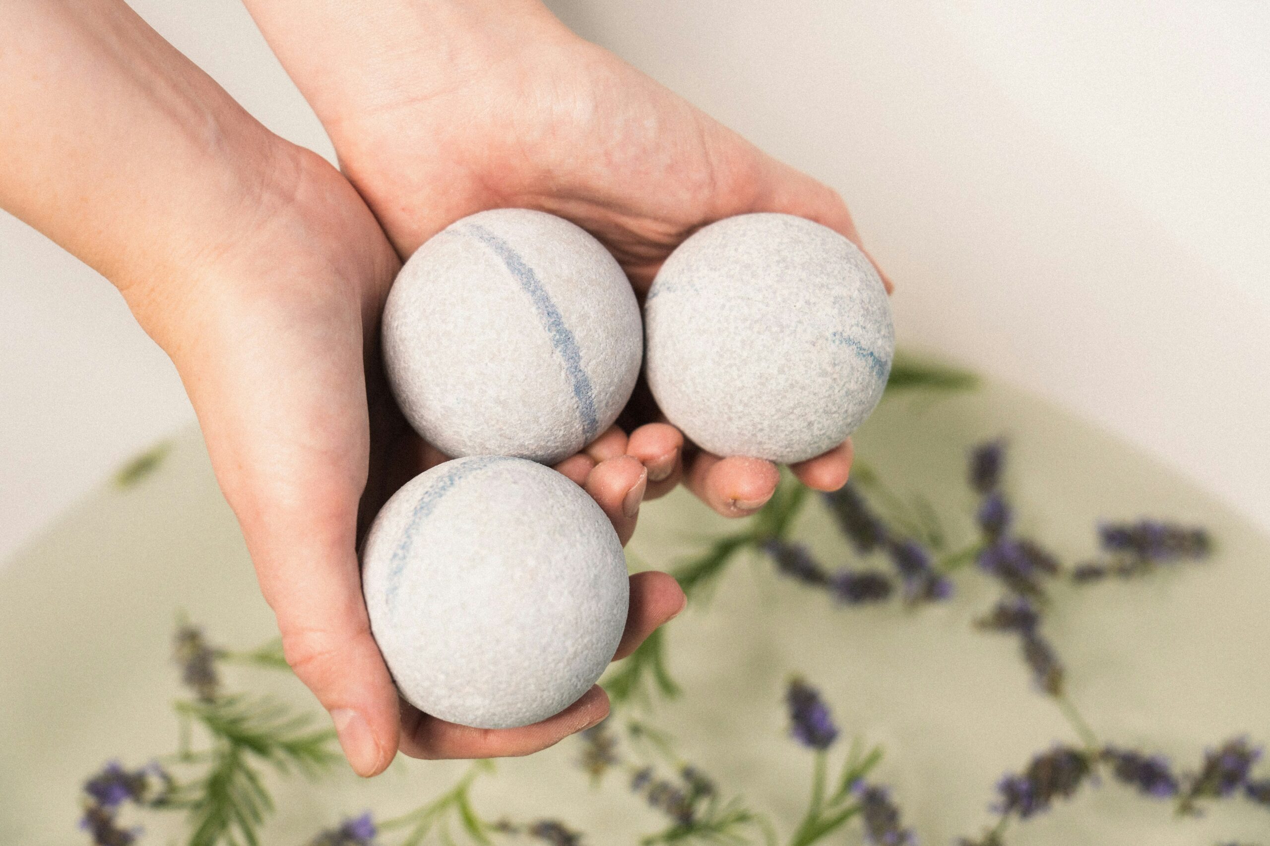 Person hält umweltfreundliche Produkte (Badebomben) über eine Badewanne.