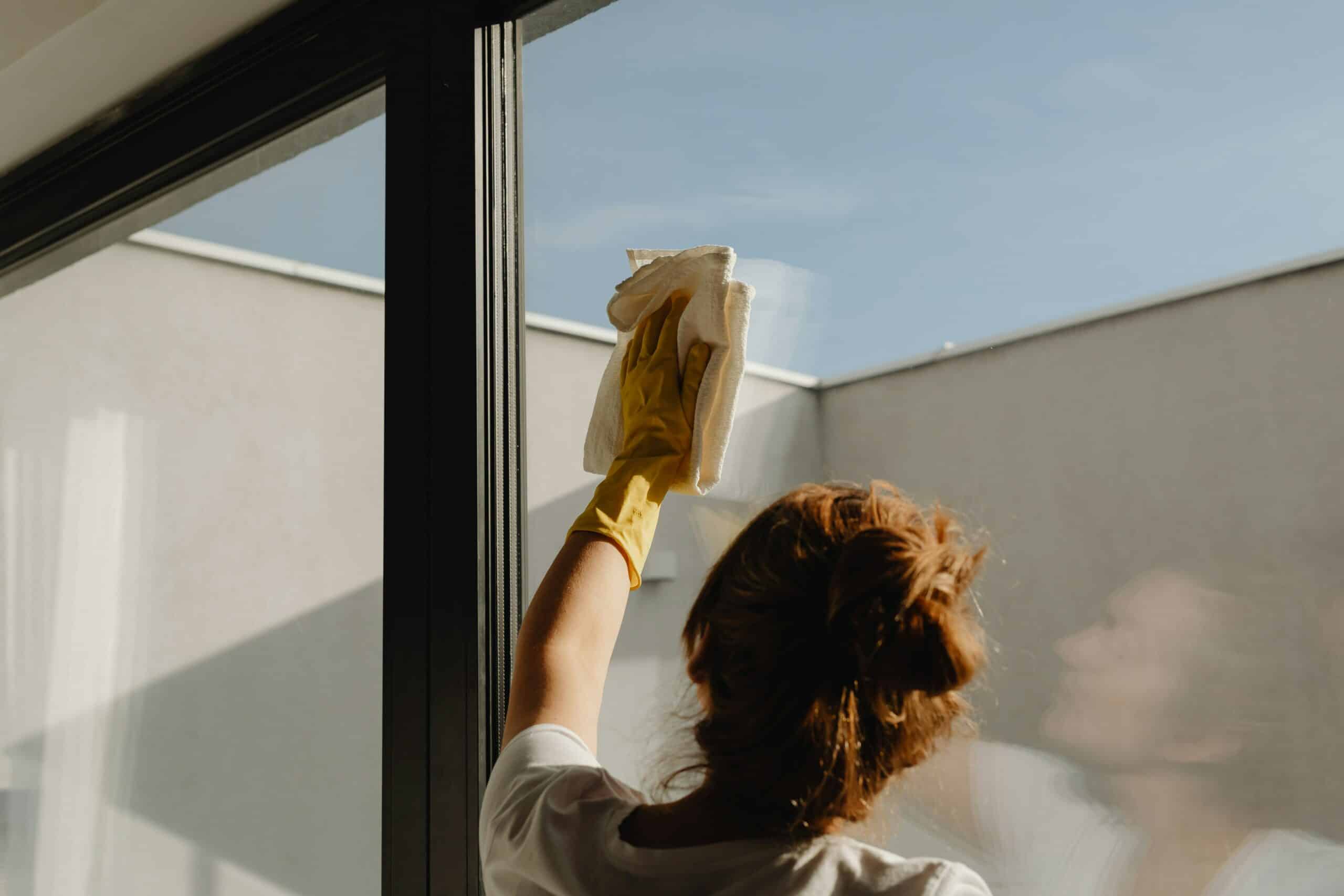 Person reinigt ein Fenster mit einem nachhaltigen Reinigungstuch und einem umweltfreundlichen Reinigungsmittel.